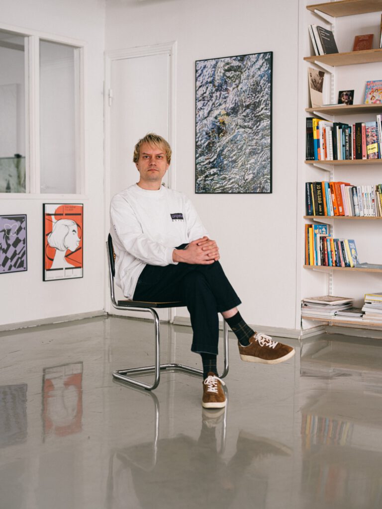Jaakko Suomalainen istuu tuolilla keskellä huonetta, seinillä tauluja ja reunassa kirjahylly.